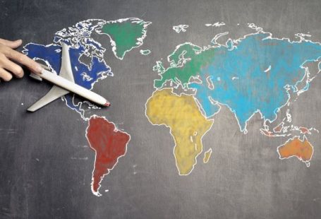 Round-the-World Trip - Top view of crop anonymous person holding toy airplane on colorful world map drawn on chalkboard