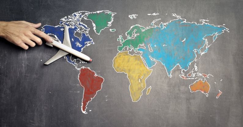 Round-the-World Trip - Top view of crop anonymous person holding toy airplane on colorful world map drawn on chalkboard