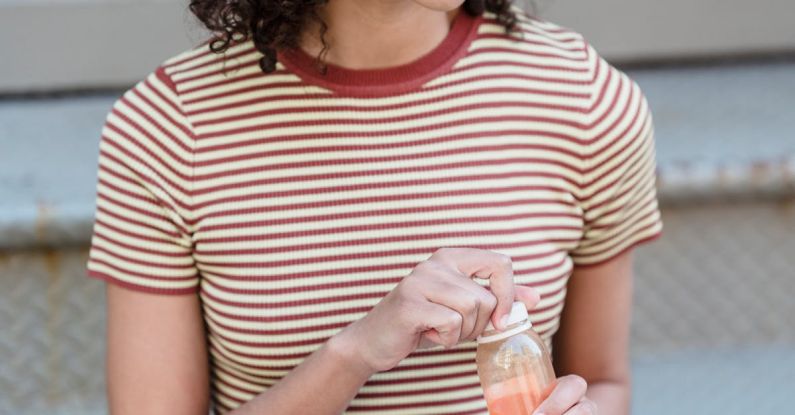 Digital Detoxes - Happy young ethnic female student with curly hair in trendy outfit smiling and looking away while drinking fresh juice sitting on stairs on street with modern laptop on knees