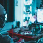 Reality TV - Side view of unrecognizable person in virtual reality helmet sitting on sofa and playing with gamepad in dark room