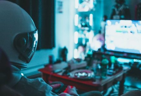 Reality TV - Side view of unrecognizable person in virtual reality helmet sitting on sofa and playing with gamepad in dark room